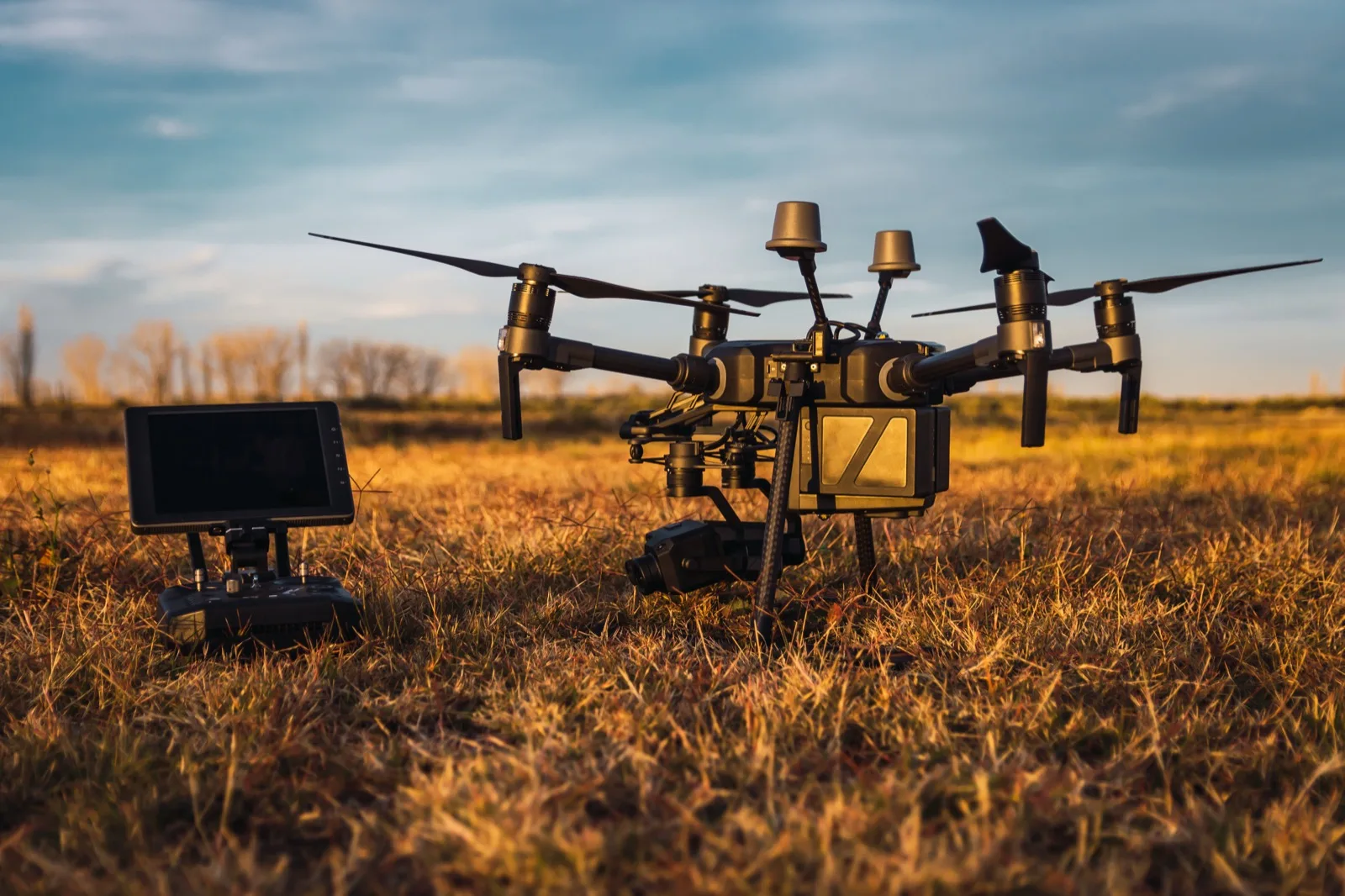 A heavy-lift drone with a gimbal camera on open ground at dusk, its ground control station alongside