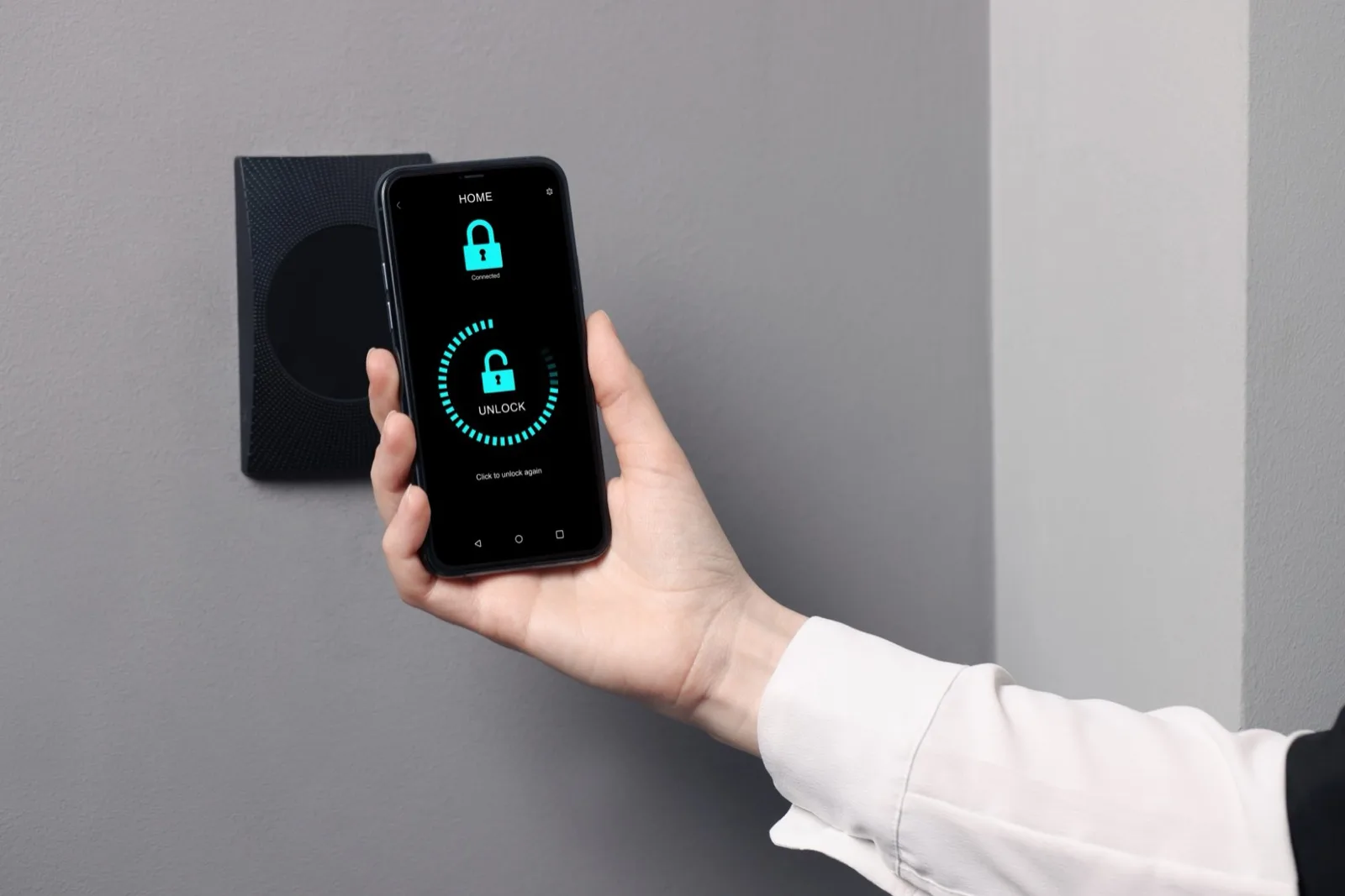 A hand holding a phone up to a wall-mounted reader, the app showing the door unlocking