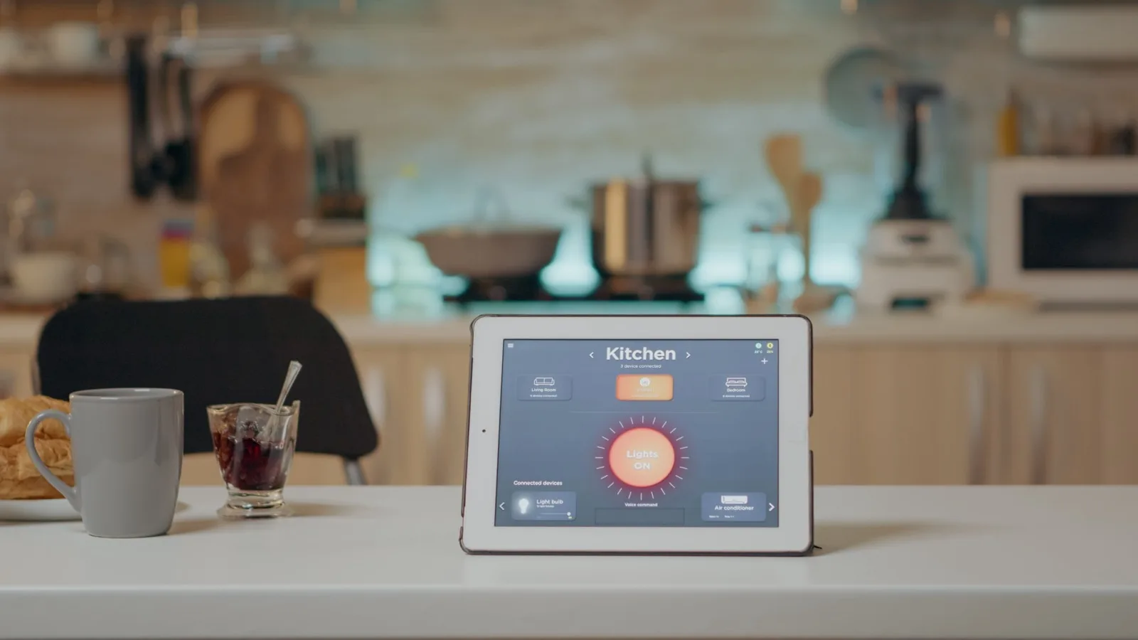 A tablet on a kitchen counter running a room-by-room home control panel, lighting and air conditioning listed as connected