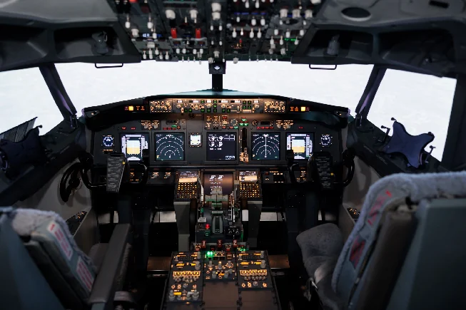 An airliner flight deck with lit instrument displays and overhead control panels