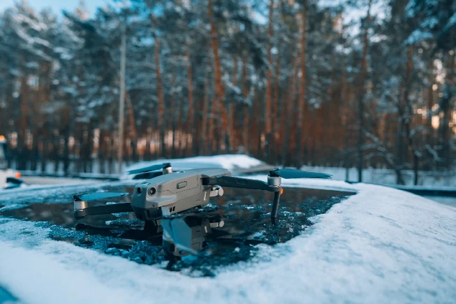 A compact quadcopter drone resting on a snow-covered surface in a pine forest